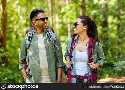 travel, tourism, hike and people concept - mixed race couple with backpacks in forest. mixed race couple with backpacks hiking in forest