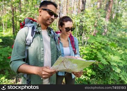 travel, tourism, hike and people concept - mixed race couple with map and backpacks in forest. mixed race couple with map and backpacks in forest