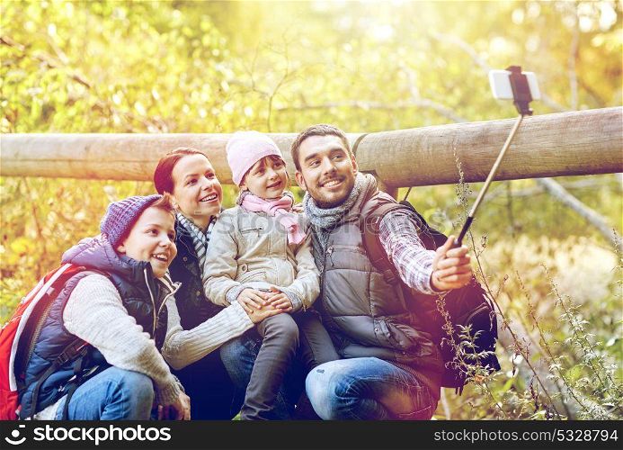 travel, tourism, hike and technoligy concept - happy family with backpacks taking picture by smartphone and selfie stick in woods. happy family with smartphone selfie stick in woods