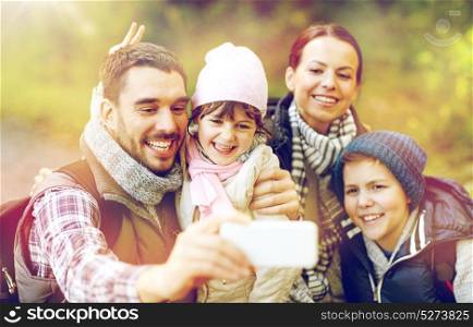 travel, tourism, hike and technology concept - happy family with backpacks taking selfie by smartphone in woods. family taking selfie with smartphone in woods