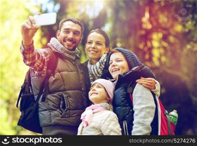 travel, tourism, hike and technology concept - happy family with backpacks taking selfie by smartphone in woods. family taking selfie with smartphone in woods