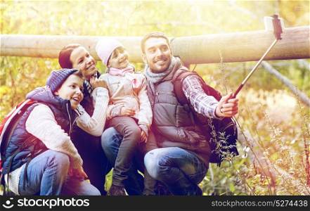 travel, tourism, hike and technology concept - happy family with backpacks taking picture by smartphone and selfie stick in woods. happy family with smartphone selfie stick in woods
