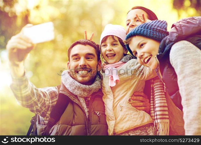 travel, tourism, hike and technology concept - happy family with backpacks taking selfie by smartphone outdoors. family taking selfie with smartphone outdoors