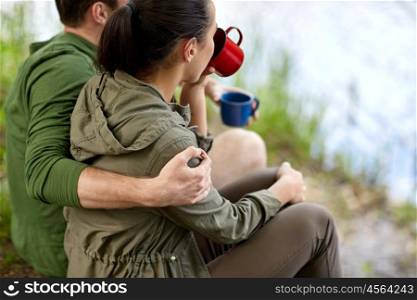 travel, tourism, hike, camping and people concept - close up of couple with cups drinking tea in nature on river bank
