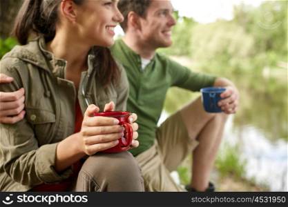 travel, tourism, hike, camping and people concept - close up of happy couple with cups drinking tea in nature on river bank