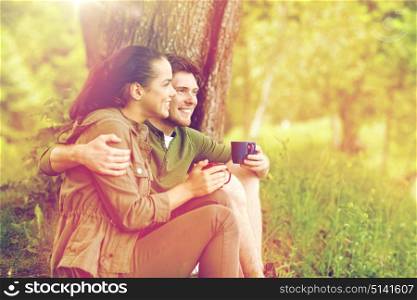 travel, tourism, hike, camping and people concept - happy couple with cups drinking tea and hugging in nature. happy couple with cups drinking tea in nature