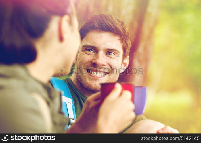 travel, tourism, hike, camping and people concept - happy couple with cups drinking tea and talking in nature. happy couple with cups drinking tea in nature