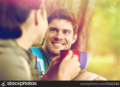 travel, tourism, hike, camping and people concept - happy couple with cups drinking tea and talking in nature. happy couple with cups drinking tea in nature