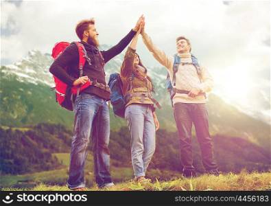 travel, tourism, hike, gesture and people concept - group of smiling friends with backpacks making high five over alpine mountains and hills background