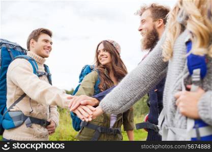 travel, tourism, hike, gesture and people concept - group of smiling friends with backpacks putting hands on top of each other