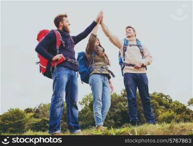 travel, tourism, hike, gesture and people concept - group of smiling friends with backpacks making high five outdoors