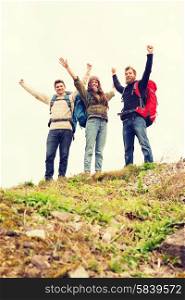 travel, tourism, hike, gesture and people concept - group of smiling friends with backpacks raising hands outdoors