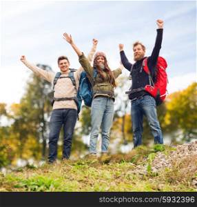 travel, tourism, hike, gesture and people concept - group of smiling friends with backpacks raising hands over natural background