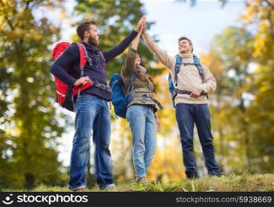 travel, tourism, hike, gesture and people concept - group of smiling friends with backpacks making high five over natural background