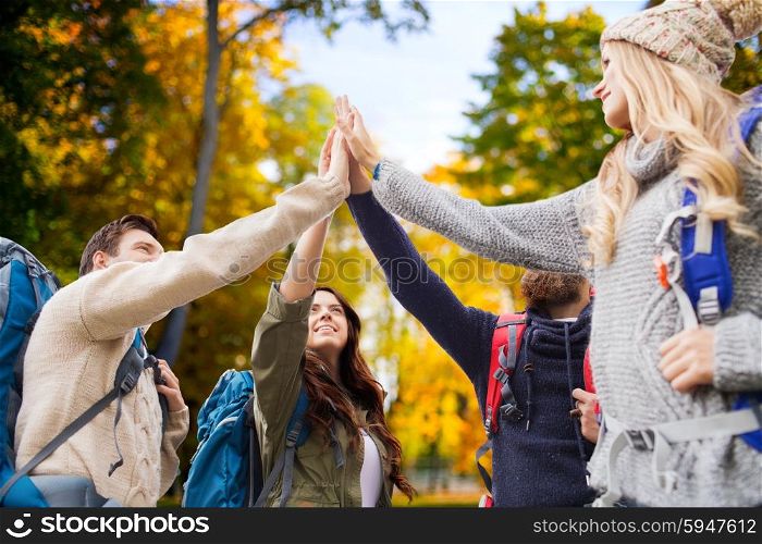 travel, tourism, hike, gesture and people concept - group of smiling friends with backpacks making high five over autumn forest background