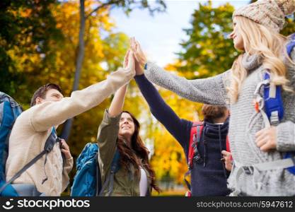 travel, tourism, hike, gesture and people concept - group of smiling friends with backpacks making high five over autumn forest background