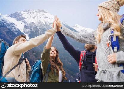 travel, tourism, hike, gesture and people concept - group of smiling friends with backpacks making high five over mountains background