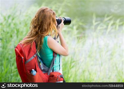 travel, tourism, hike, hobby and people concept - young woman with backpack and camera photographing outdoors