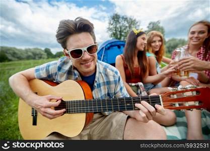 travel, tourism, hike, leisure and people concept - happy man with friends playing guitar at camping