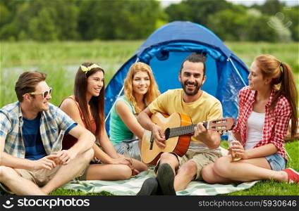 travel, tourism, hike, picnic and people concept - group of happy friends with tent and drinks playing guitar at camping