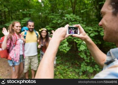travel, tourism, hike, technology and people concept - close up of happy young man photographing friends with backpacks by smartphone outdoors