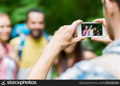 travel, tourism, hike, technology and people concept - close up of man photographing friends with backpacks by smartphone outdoors