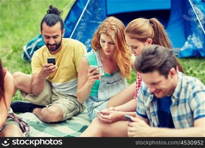 travel, tourism, hike, technology and people concept - group of friends with smartphone and tent at camping