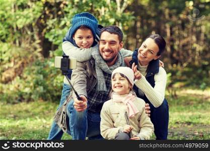 travel, tourism, hike, technology and people concept - happy family taking picture with smartphone selfie stick in woods. happy family with smartphone selfie stick in woods