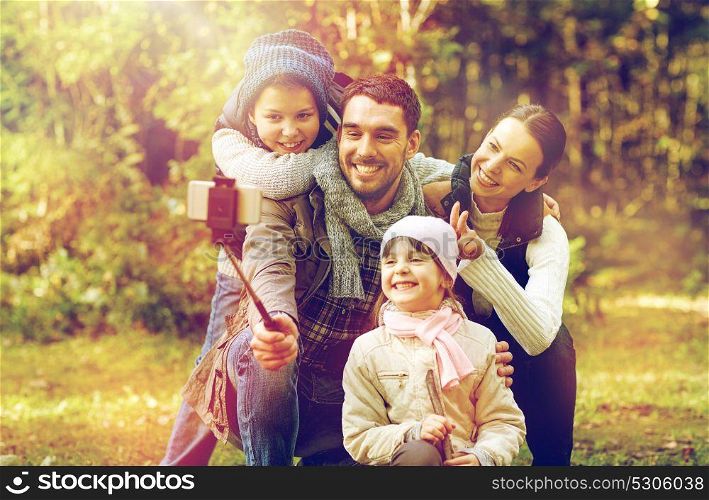 travel, tourism, hike, technology and people concept - happy family taking picture with smartphone selfie stick in woods. happy family with smartphone selfie stick in woods