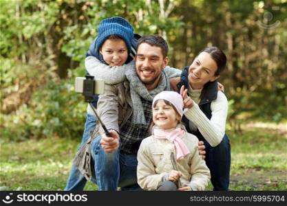 travel, tourism, hike, technology and people concept - happy family taking picture with smartphone selfie stick in woods