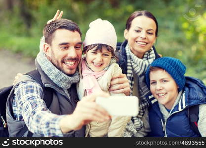 travel, tourism, hike, technology and people concept - happy family with backpacks taking selfie by smartphone in woods