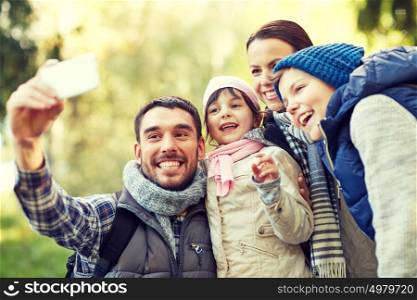 travel, tourism, hike, technology and people concept - happy family with backpacks taking selfie by smartphone outdoors. family taking selfie with smartphone outdoors