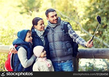 travel, tourism, hike, technology and people concept - happy family with backpacks taking picture by smartphone and selfie stick in woods. happy family with smartphone selfie stick in woods