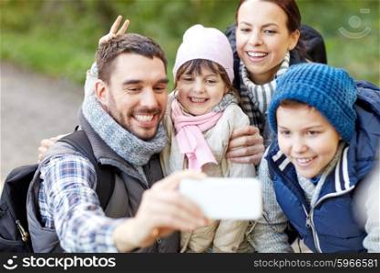 travel, tourism, hike, technology and people concept - happy family with backpacks taking selfie by smartphone in woods