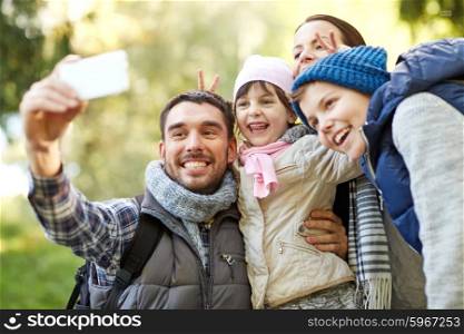 travel, tourism, hike, technology and people concept - happy family with backpacks taking selfie by smartphone outdoors