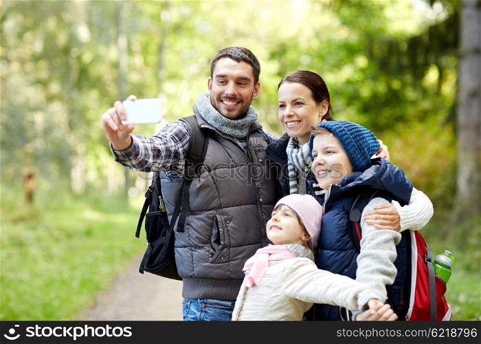 travel, tourism, hike, technology and people concept - happy family with backpacks taking selfie by smartphone in woods