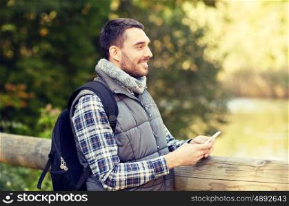 travel, tourism, hike, technology and people concept - happy man with backpack and smartphone outdoors