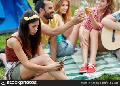 travel, tourism, hike, technology and people concept - young woman with smartphone and friends at camping