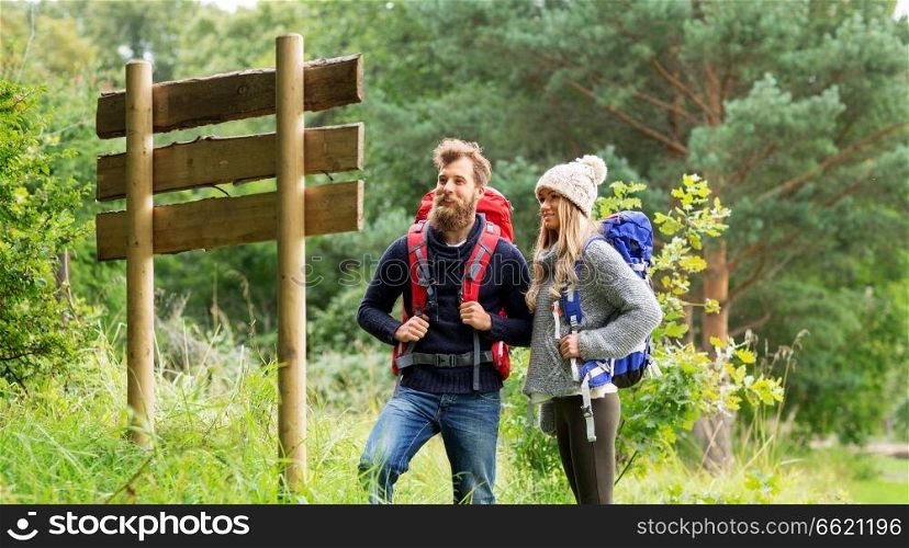travel, tourism, hiking and people concept - couple of travelers with backpacks looking at signpost. couple of travelers with backpacks at signpost