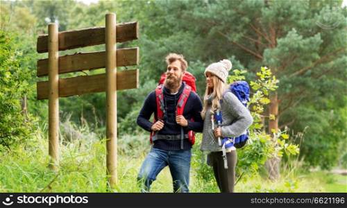 travel, tourism, hiking and people concept - couple of travelers with backpacks looking at signpost. couple of travelers with backpacks at signpost