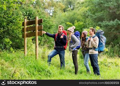 travel, tourism, hiking and people concept - group of happy friends or travelers with backpacks looking at signpost. hiking friends with backpacks at signpost