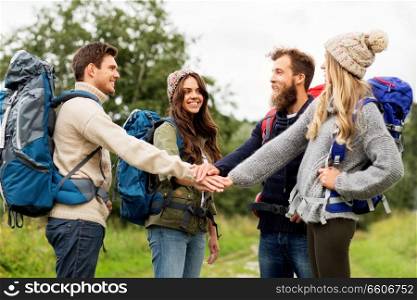 travel, tourism, hiking and people concept - group of smiling friends or travelers with backpacks stacking hands outdoors. friends with backpacks hiking and stacking hands