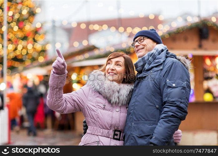 travel, tourism, holidays and people concept - happy senior couple hugging at christmas market on town hall square in tallinn, estonia. happy senior couple hugging at christmas market