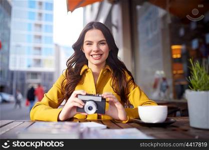 travel, tourism, photography, leisure and people concept - happy young tourist woman or teenage girl with film camera and guidebook drinking cocoa at city street cafe terrace
