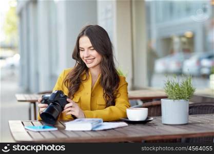 travel, tourism, photography, leisure and people concept - happy young tourist woman or teenage girl with digital camera photographing and drinking cocoa at city street cafe terrace