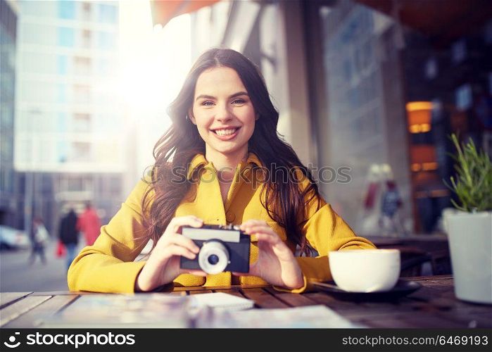 travel, tourism, photography, leisure and people concept - happy young tourist woman or teenage girl with film camera and guidebook drinking cocoa at city street cafe terrace. happy tourist woman with camera at city cafe