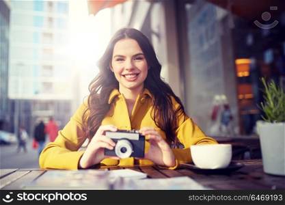 travel, tourism, photography, leisure and people concept - happy young tourist woman or teenage girl with film camera and guidebook drinking cocoa at city street cafe terrace. happy tourist woman with camera at city cafe