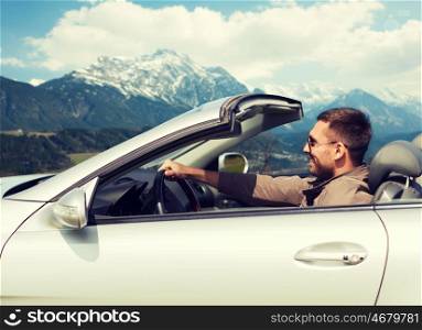 travel, tourism, road trip, transport and people concept - happy man driving cabriolet car over mountains background