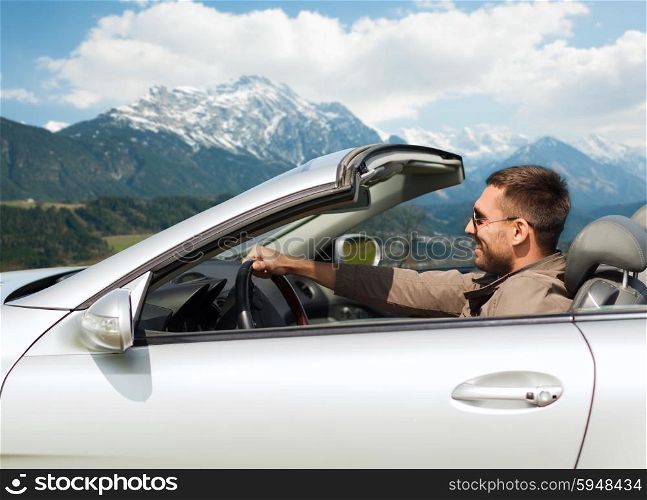 travel, tourism, road trip, transport and people concept - happy man driving cabriolet car over mountains background