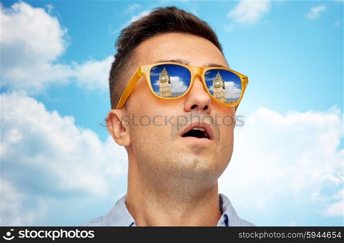 travel, tourism, sightseeing, emotions and people concept - face of man in sunglasses looking at big ben tower over blue sky and clouds background